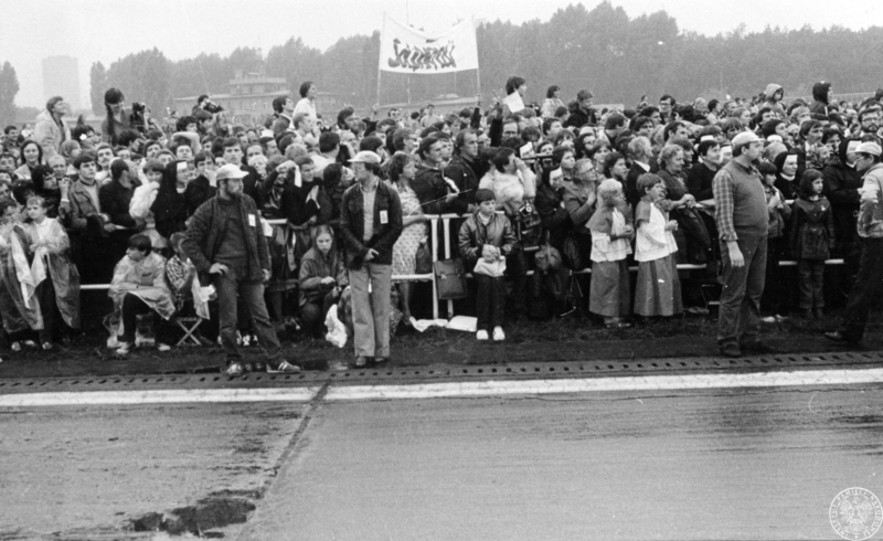 Fot. nr 2. Wierni zgromadzeni na lotnisku w dzielnicy Muchowiec czekają na przybycie Jana Pawła II. W centrum kadru widoczny jest transparent, na którym widnieje napis "SOLIDARNOŚĆ". 20 VI 1983 r. Sygnatura: IPNKa-7-7-2-8