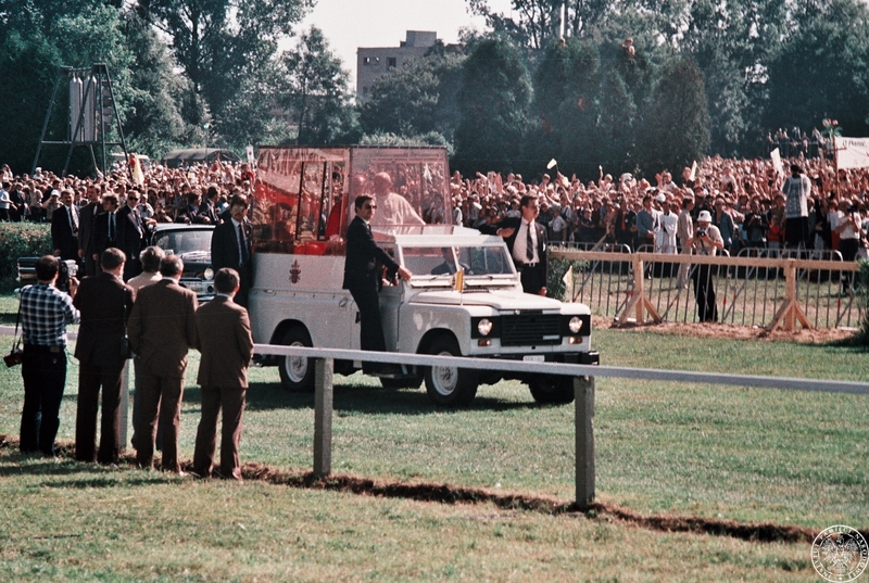 Fot. nr 5. Jan Paweł II w papamobile w otoczeniu ochroniarzy wjeżdża na hipodrom na Partynicach pozdrawiany przez wiernych zgromadzonych w sektorach. 21 VI 1983 r.  Sygnatura: IPNBU-7-14-13-409