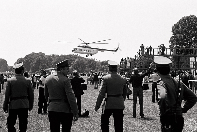 Fot. nr 16.  Śmigłowiec MI-8 z Janem Pawłem II na pokładzie ląduje na hipodromie na Partynicach pozdrawiany przez wiernych. Na pierwszym planie czterech milicjantów. 21 VI 1983 r.  Sygnatura: IPNBU-7-14-13-1059