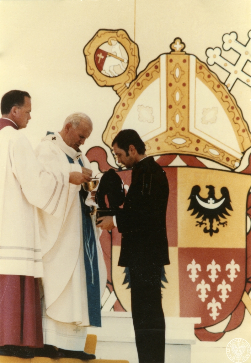 Obok papieża mistrz papieskich ceremonii liturgicznych ks. John Magee (1L). W tle herb Diecezji wrocławskiej.