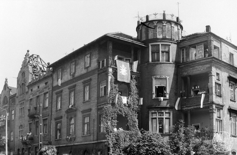 Fot. nr 7. Jeden z budynków Krakowa przy krakowskich Błoniach przystrojony flagami i transparentem z herbem papieskim. Na balkonach i oknach wierni. 22 VI 1983 r. Sygnatura: IPN Rz 739/1/31